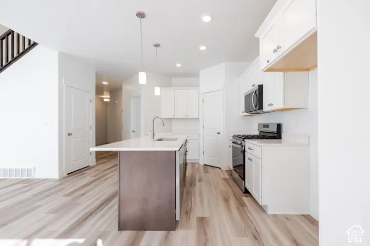 Kitchen featuring light wood-finish flooring, white cabinetry, stainless steel appliances, a center island with sink, and recessed lighting