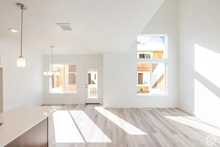 Vaulted ceiling with high windows, wood-finish flooring, white walls, kitchen island with a light-colored countertop, and a glass-paneled door