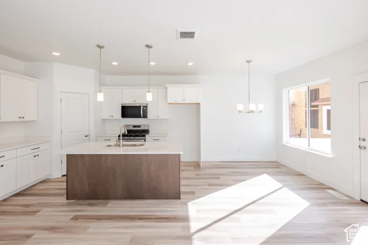 Open-concept living area featuring wood-finish flooring, a kitchen island with pendant lighting, white cabinetry, integrated stainless steel appliances, and a modern chandelier