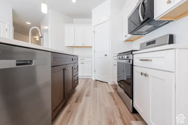 Kitchen featuring white cabinetry, a dark wood-finish island, light-toned wood-finish flooring, and stainless steel appliances