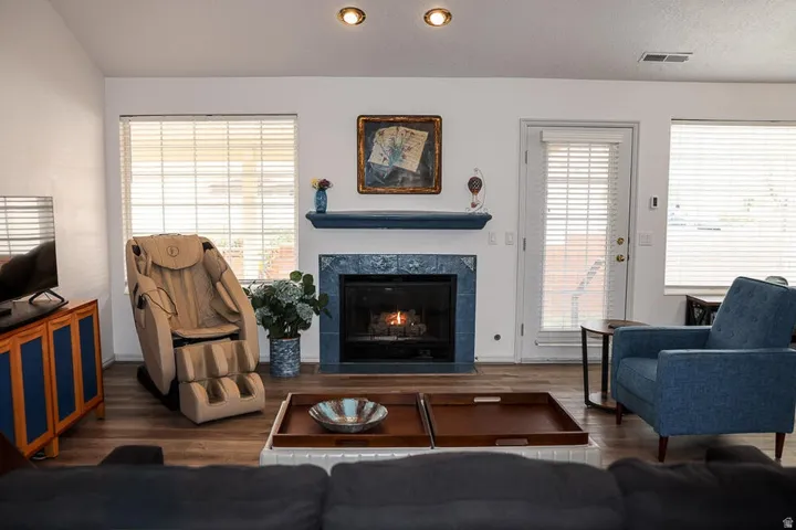 Living area featuring a fireplace with blue tile surround and mantel, wood-finish flooring, recessed lighting, and a white paneled door