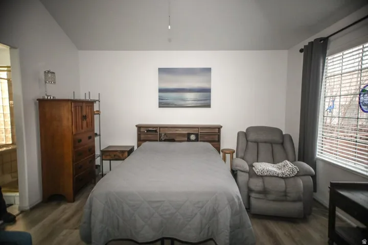 Vaulted ceilings enhance this room featuring wood-finish flooring and a window with blinds and drapes