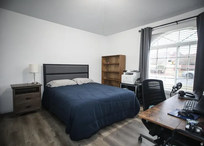 Spacious room featuring wood-finish flooring, a contemporary headboard, and a large arched window with blinds