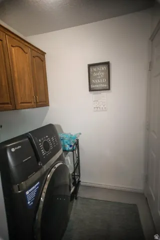 Dedicated laundry area featuring overhead wood-finish cabinetry, a white wall finish, and durable flooring