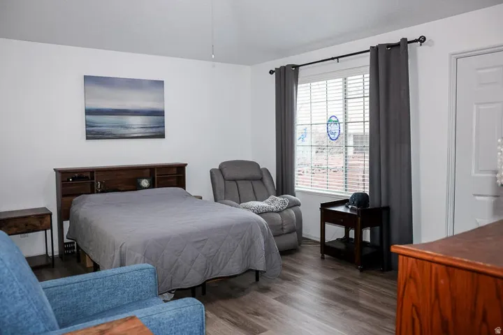 Spacious room featuring wood-finish flooring, a vaulted ceiling, and a large window with blinds