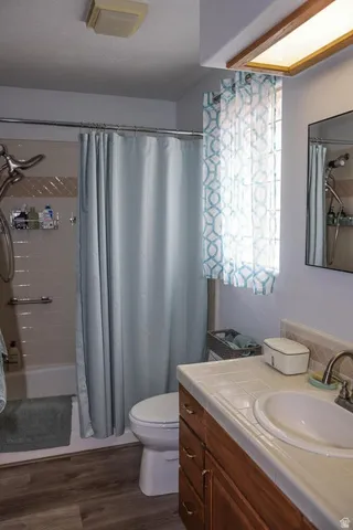 Full bathroom featuring a tub/shower combination, wood-finish flooring, a wood vanity with a tile countertop, a single basin sink, and an overhead light fixture