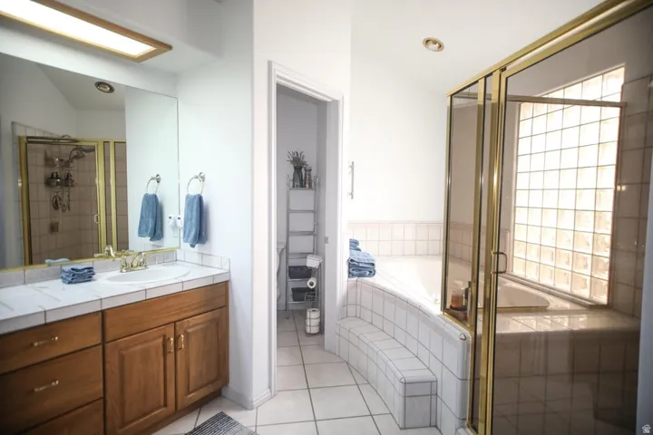 Bathroom featuring a wood-finish vanity with tile countertop, an undermount sink, and a large mirror