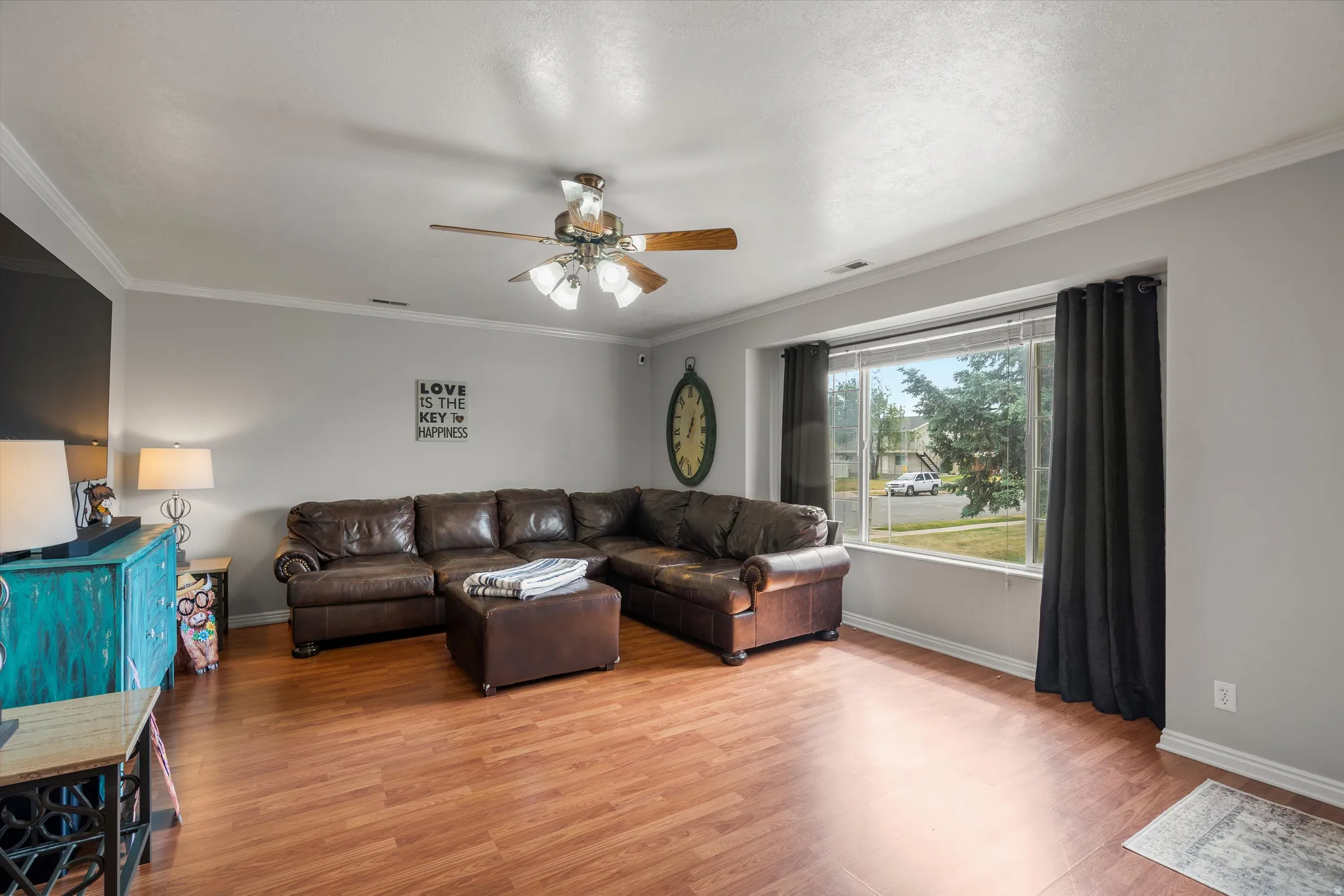 Spacious living area featuring wood-finish flooring, a large picture window with drapes, and a ceiling fan with integrated lighting