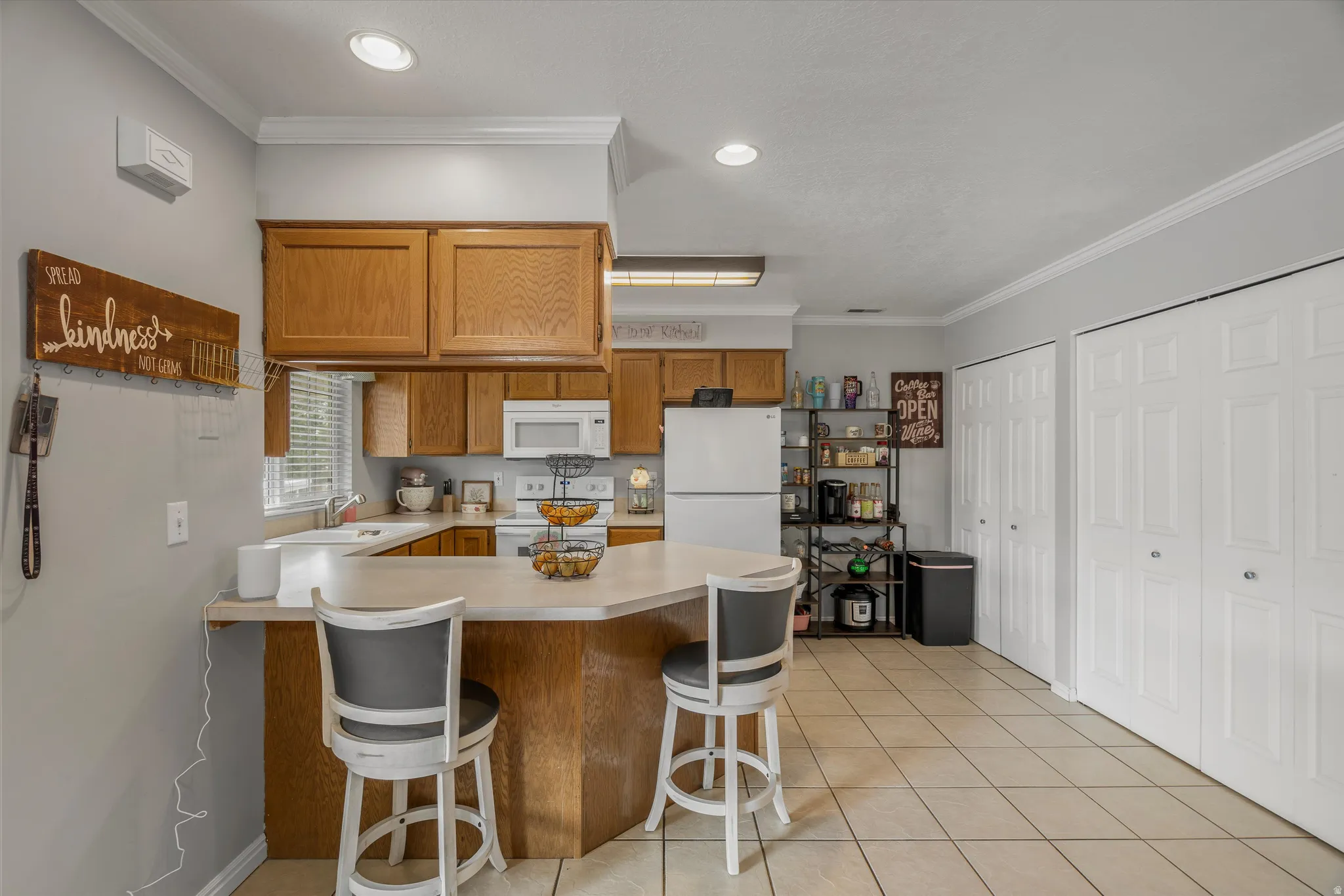 Kitchen featuring a peninsula, wood cabinetry, white appliances, and tiled flooring