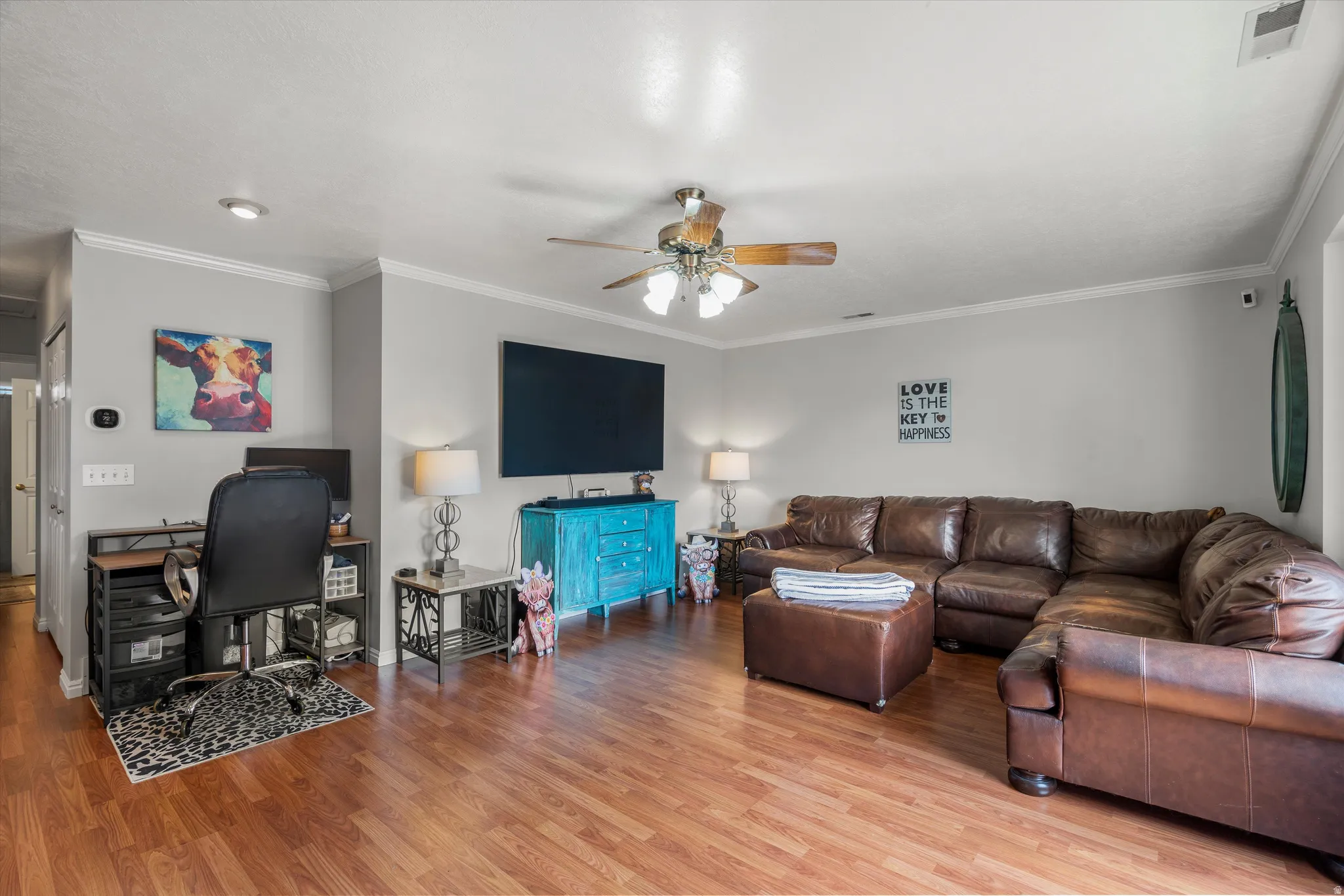Spacious living area featuring laminate flooring, light gray walls, and white crown molding