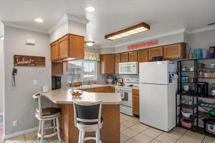Kitchen featuring a breakfast bar with seating, wood cabinetry, white appliances, and tiled flooring