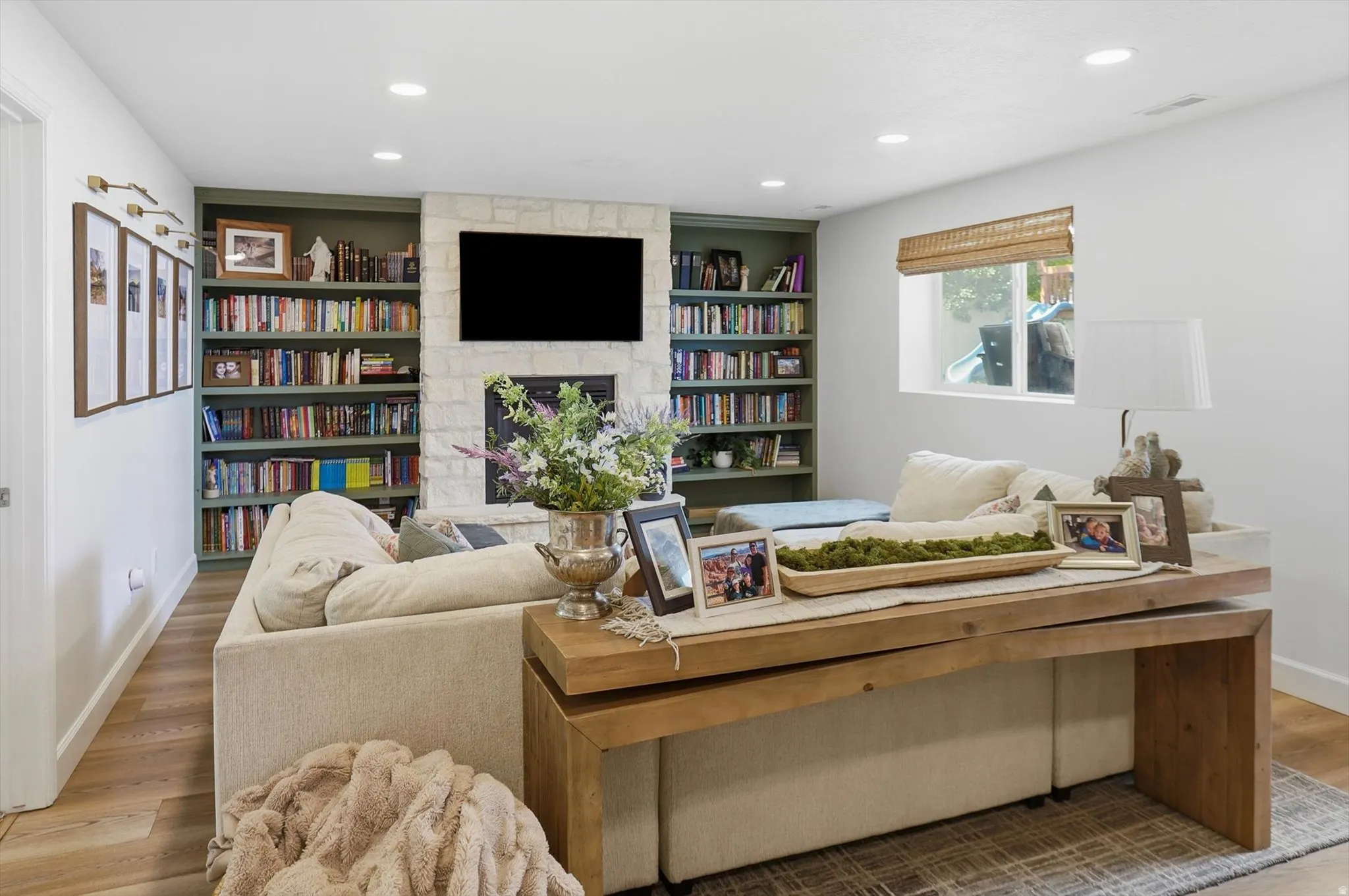Living area featuring a stone fireplace with built-in shelving, wood-finish flooring, and recessed lighting