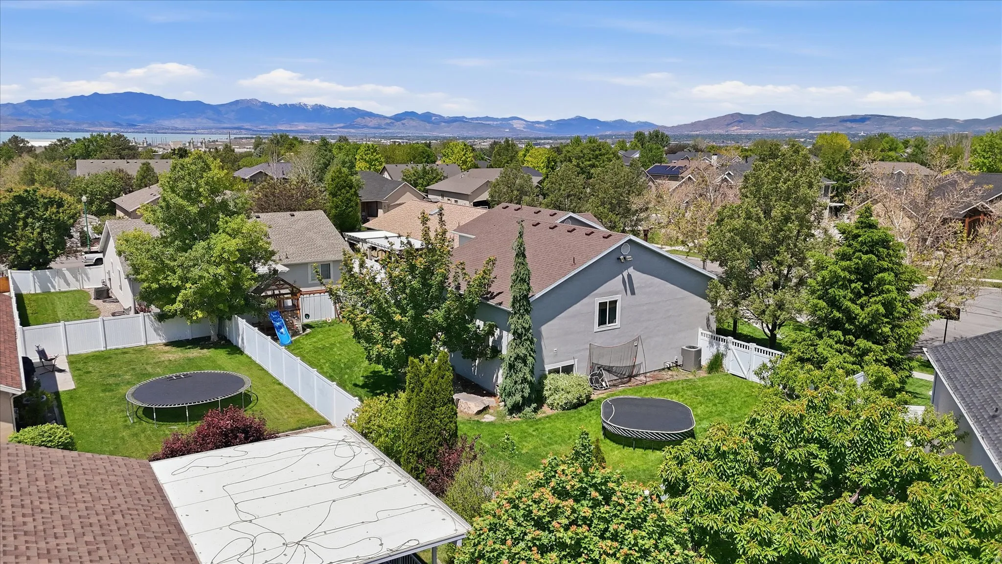 Expansive residential property with a green lawn, established trees, and white privacy fencing