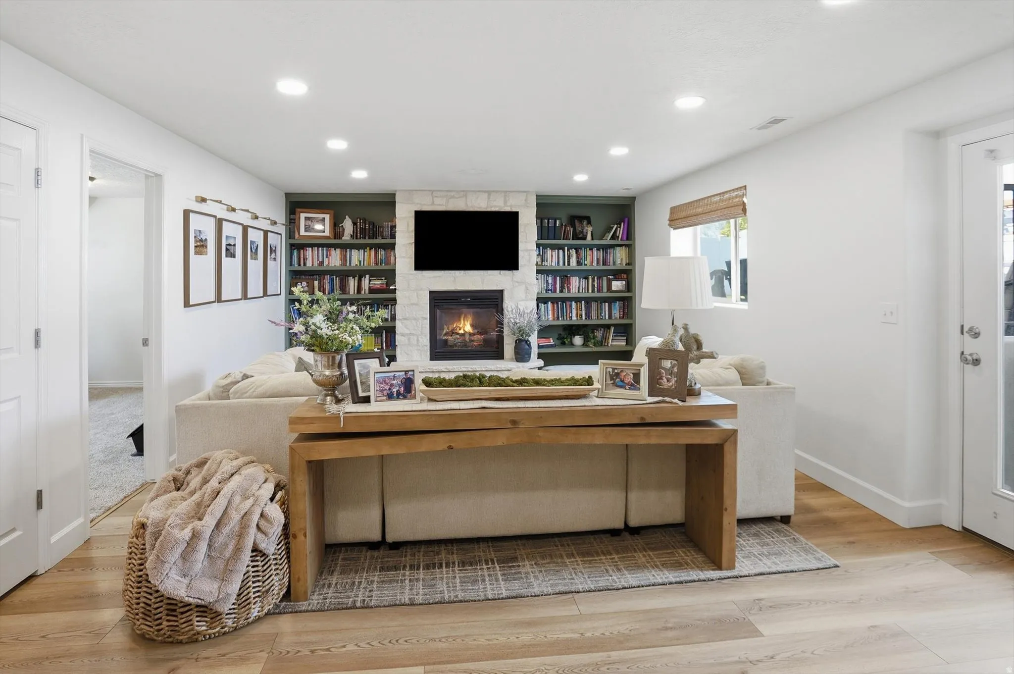 Living area featuring a stone-clad fireplace with a mounted television, built-in shelving, recessed lighting, and wood-finish flooring