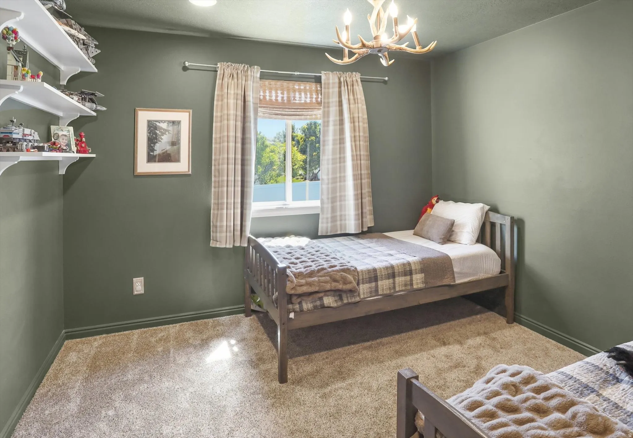 Carpeted room featuring a window with plaid curtains, built-in wall shelving, green painted walls, and an antler-style ceiling light fixture
