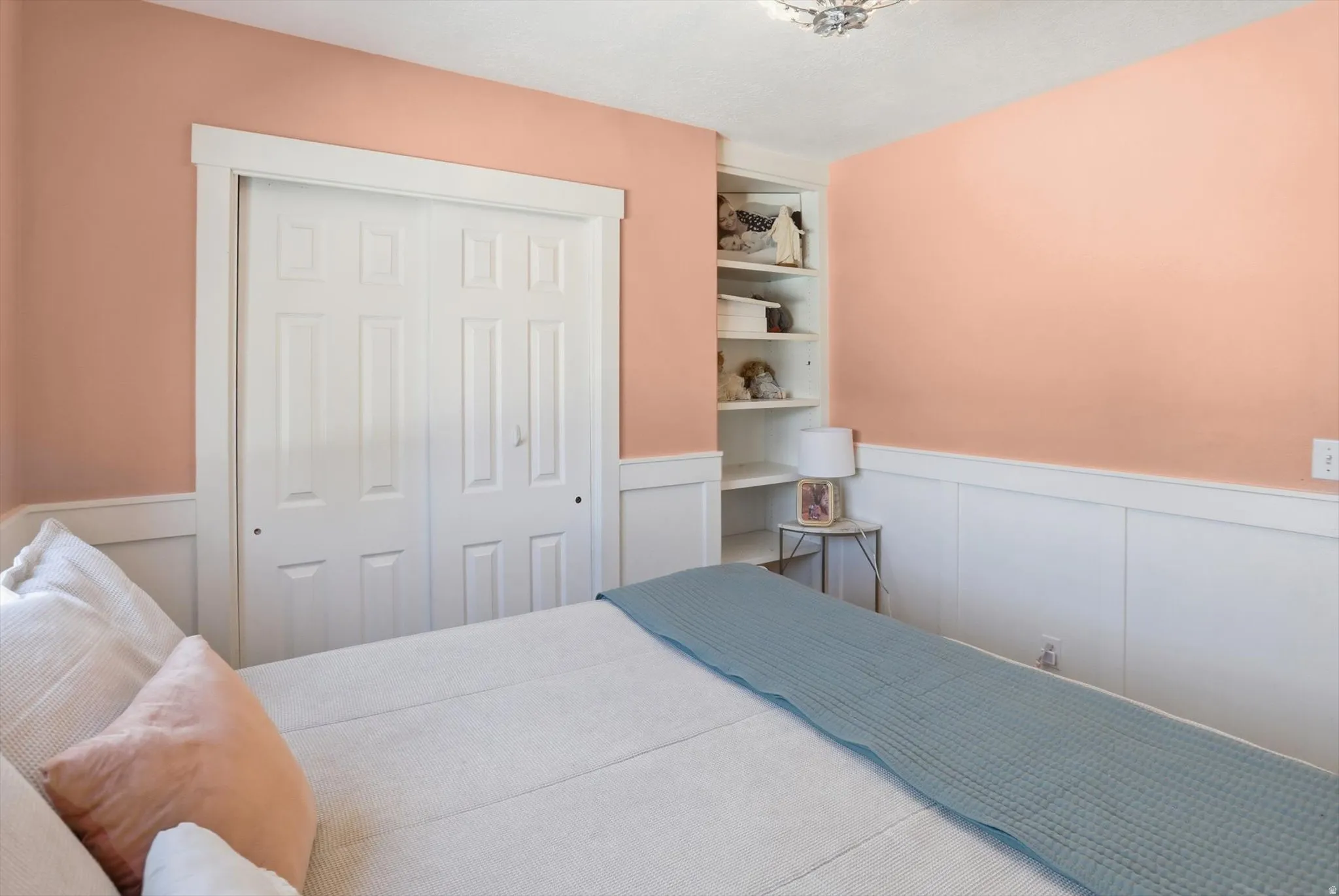 Interior space featuring two-panel bifold closet doors, built-in shelving, white wainscoting, and a ceiling-mounted light fixture