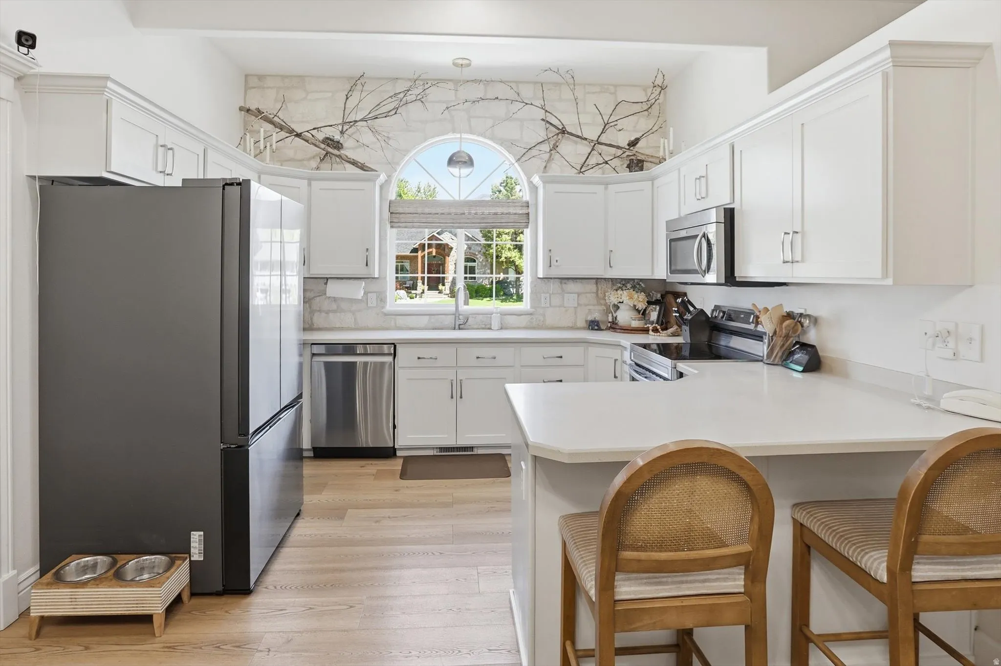 Modern kitchen featuring white cabinetry, light countertops, stainless steel appliances, and wood-finish flooring