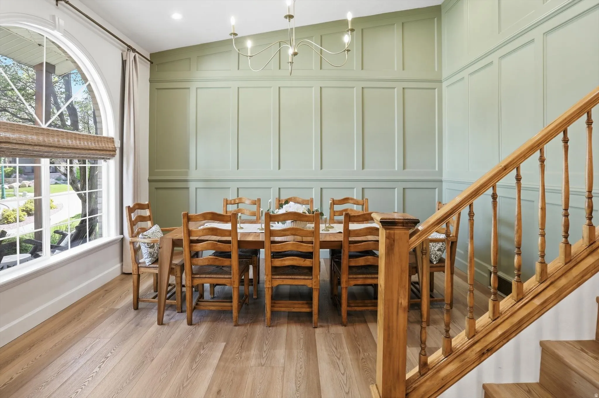 Dining area featuring wood-finish flooring, a large arched window with grid detailing, and decorative wainscoting on the walls
