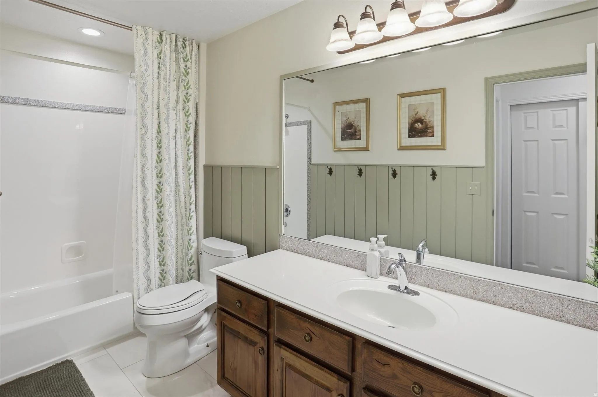 Bathroom featuring a wood-finish vanity with a white countertop and integrated sink, a large mirror, and a white tub with shower