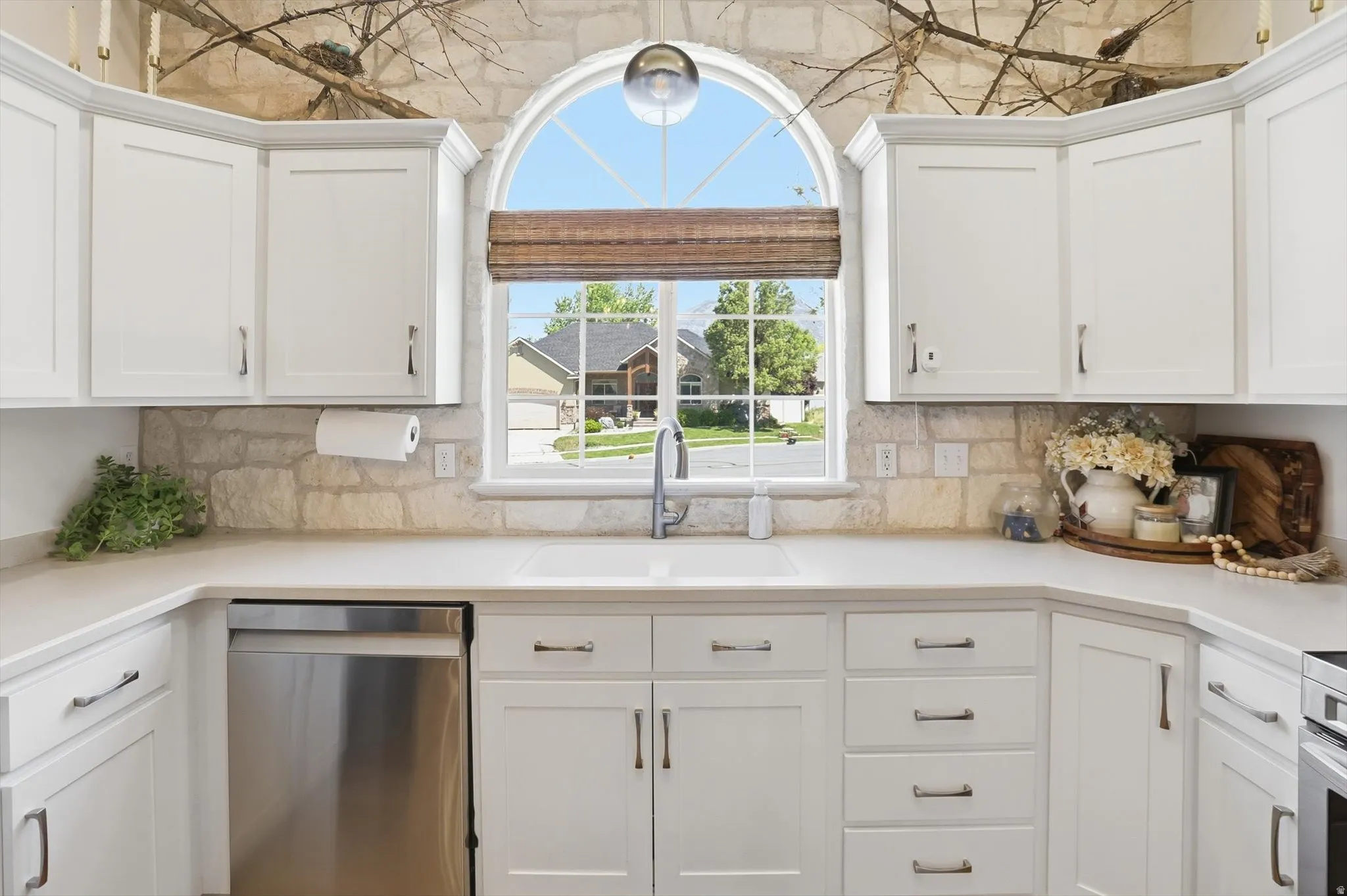 Kitchen featuring an arched window, white cabinetry, integrated sink, stainless steel dishwasher, and stone backsplash