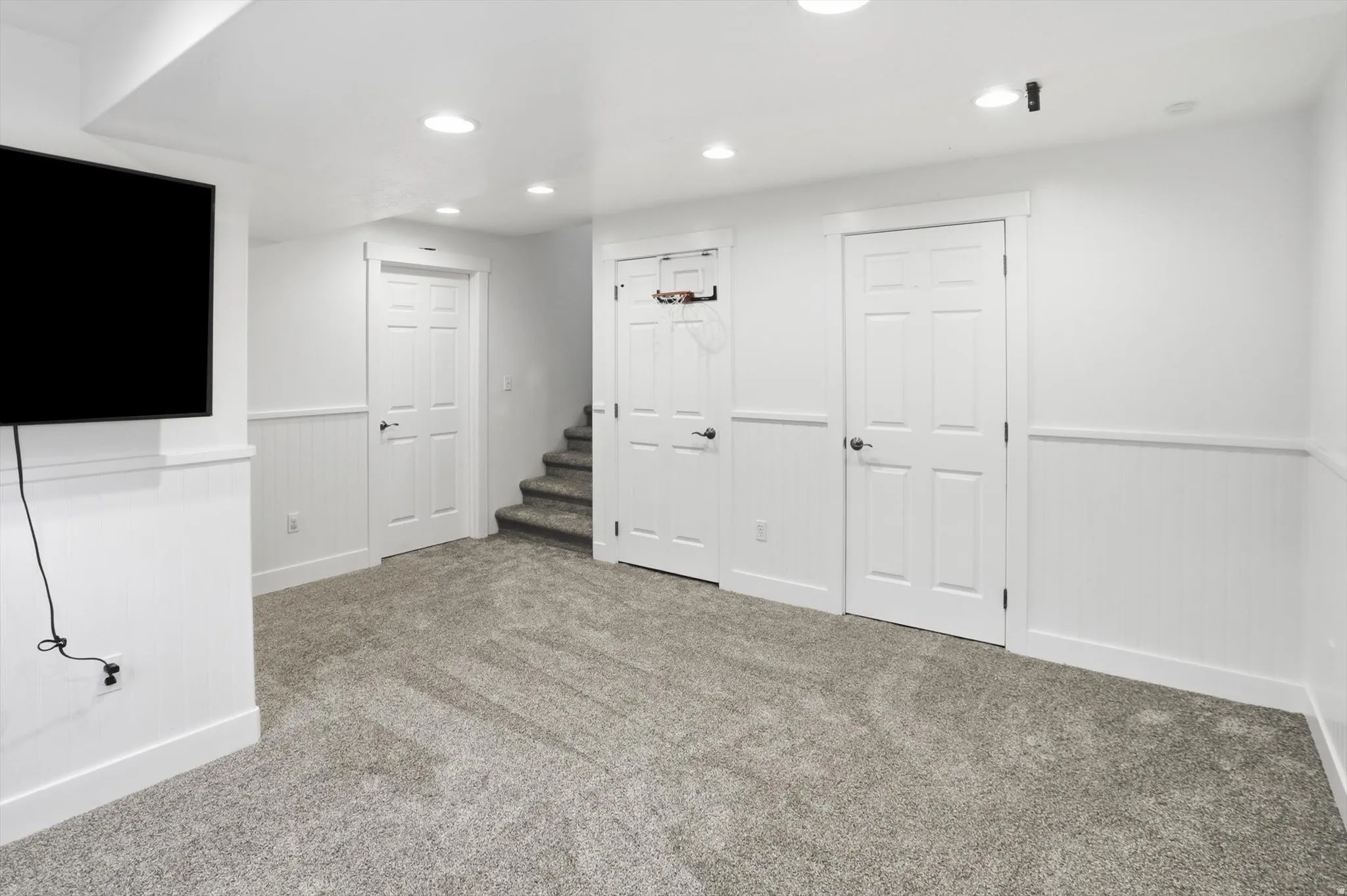 Finished room featuring gray carpeting, white wainscoting, recessed lighting, and white paneled doors