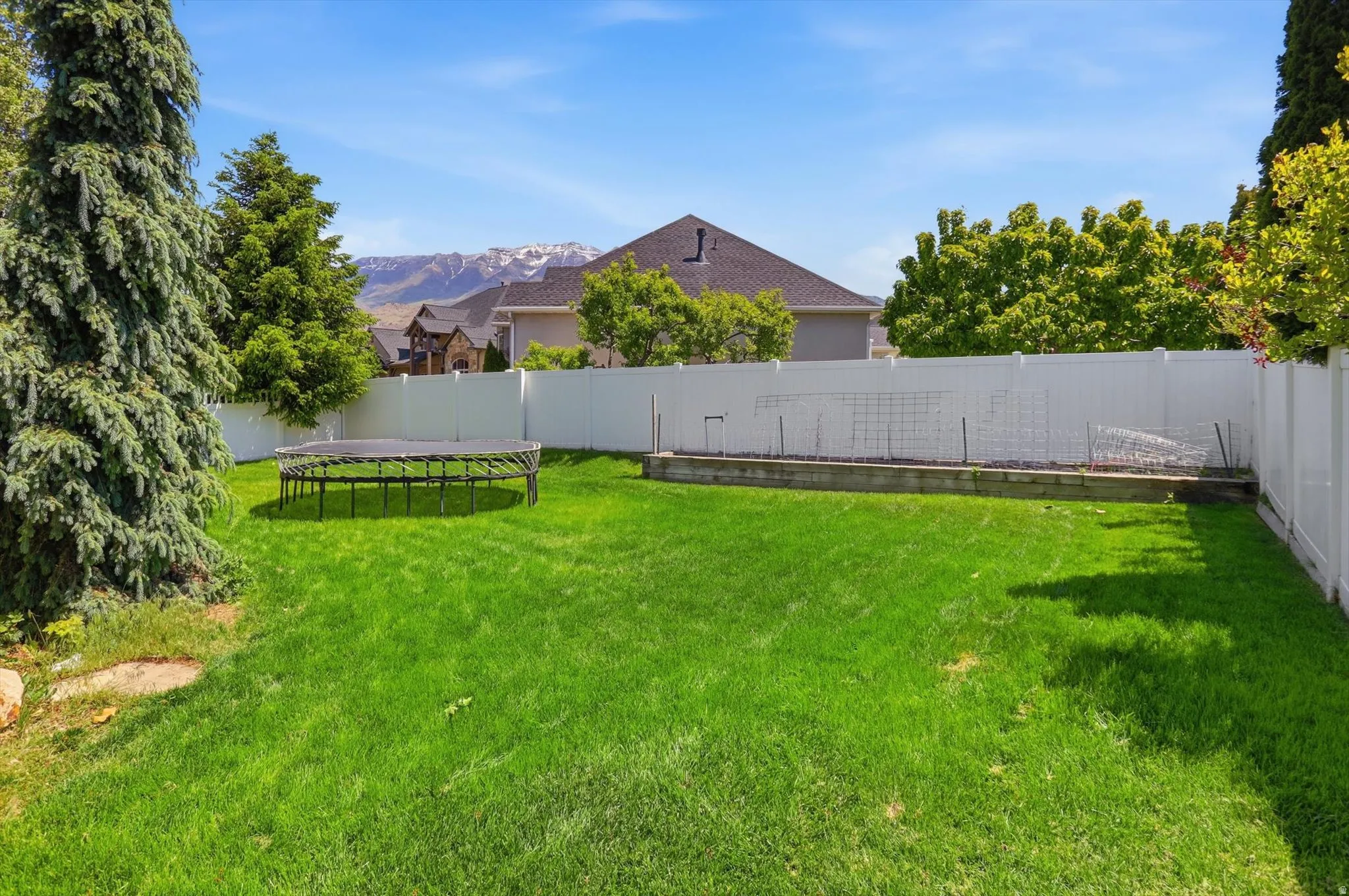 Expansive backyard featuring a lush green lawn, mature perimeter trees, a white privacy fence, and a raised garden bed