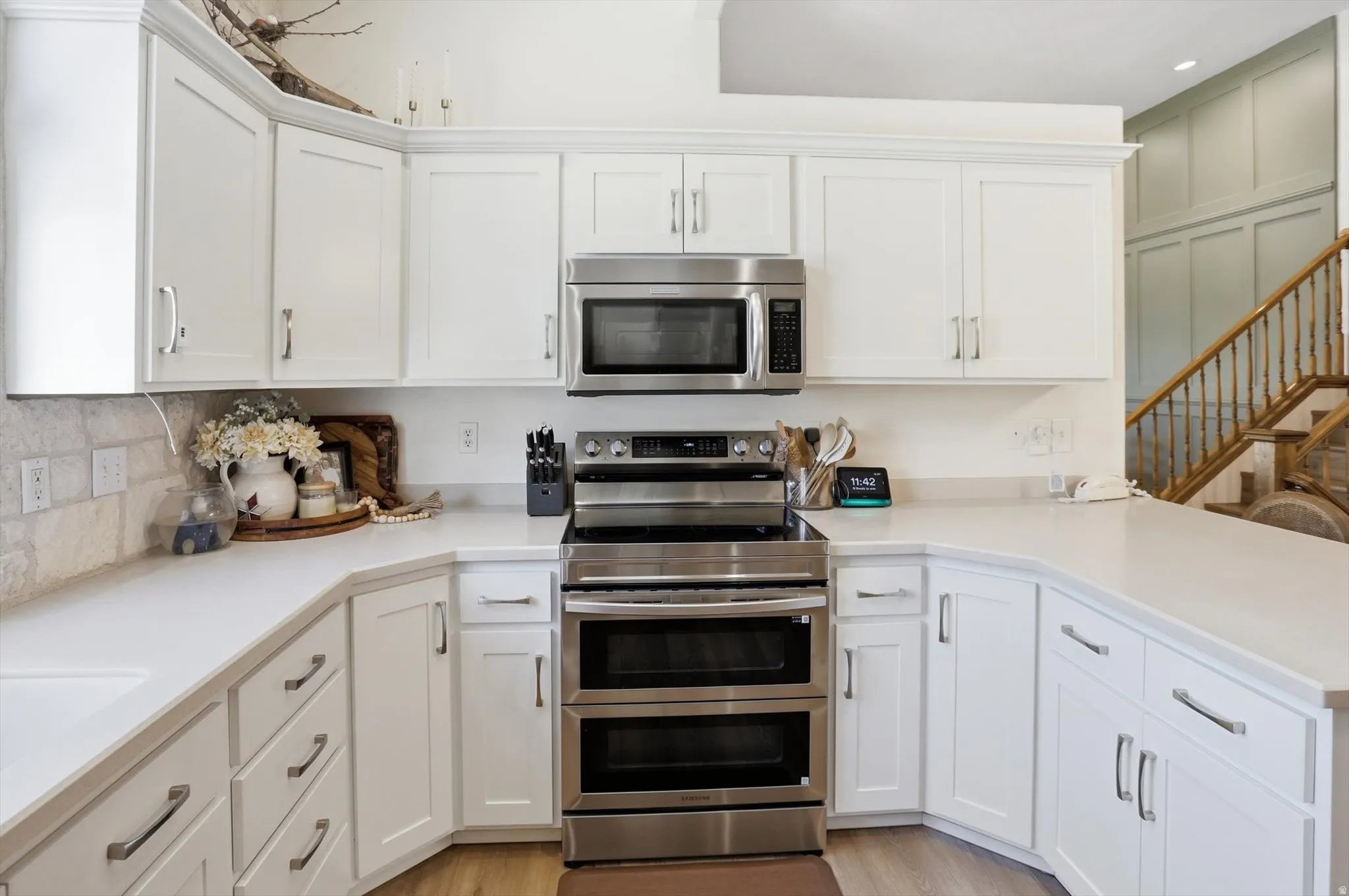 Modern kitchen featuring white shaker cabinetry, stainless steel appliances, light-toned countertops, and a stone-finish tile backsplash