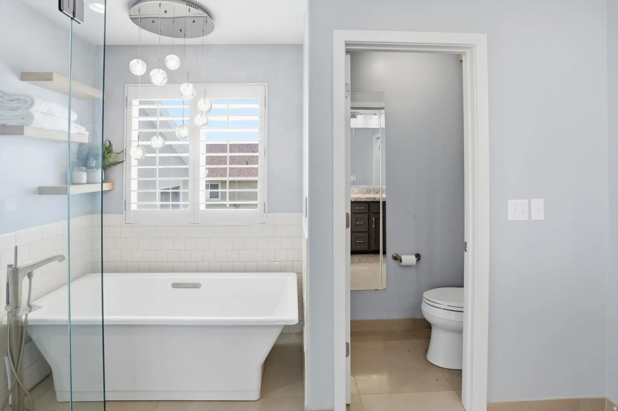 Freestanding soaking tub with a modern floor-mounted faucet, white subway tile surround, and plantation shutters