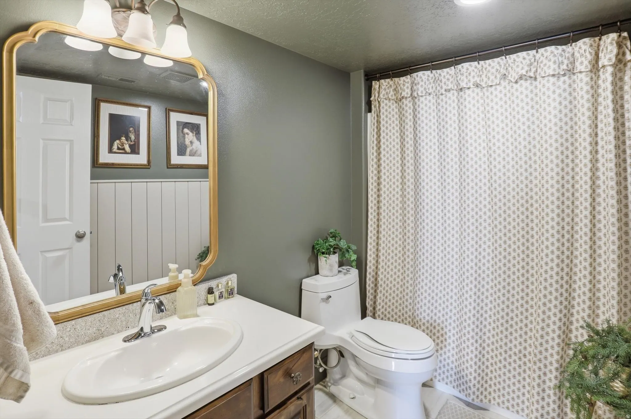 Bathroom featuring a wood-finish vanity with a white countertop and integrated sink, a large framed mirror, and a full shower with a patterned curtain