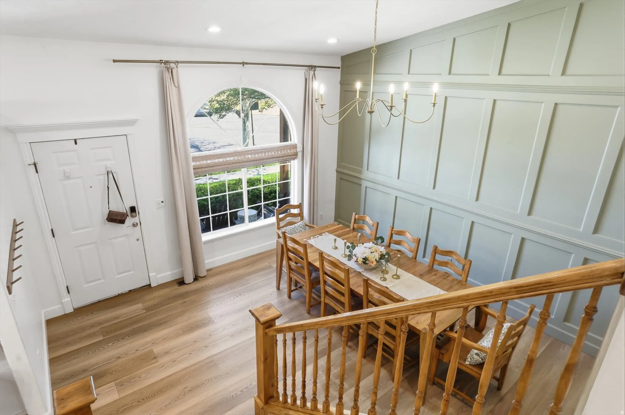 Entryway and dining area featuring light wood-finish flooring, a decorative arched window, and wainscoting