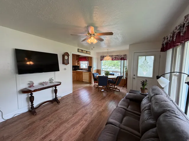 Living area featuring wood-finish flooring, white paneling, and a ceiling fan with integrated lighting
