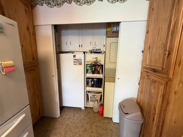 Utility closet featuring a stacked washer and dryer, additional cabinetry, and an adjacent refrigerator within a wood-paneled room