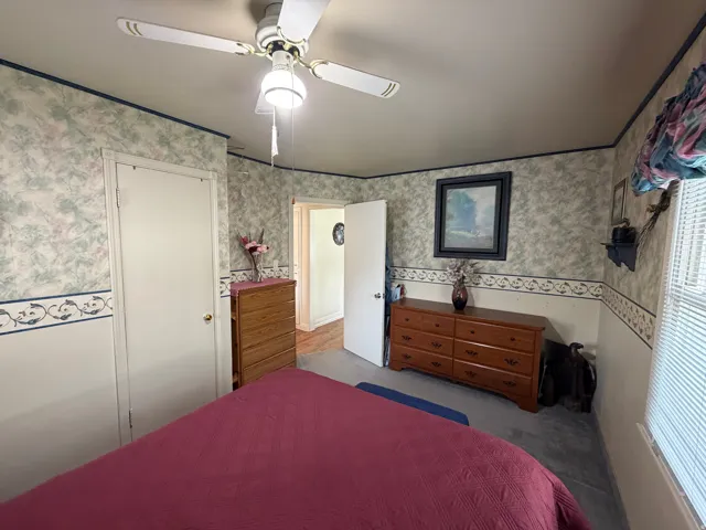 Carpeted interior room featuring a ceiling fan with integrated lighting, a window with horizontal blinds, and a white interior door