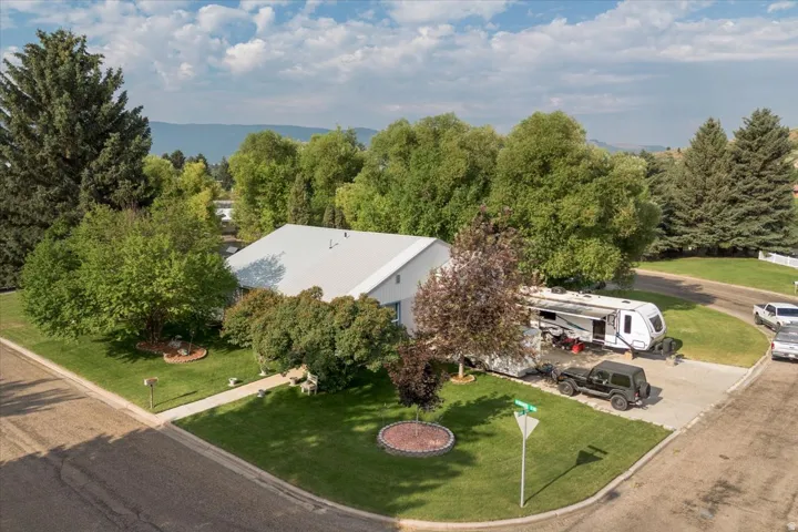 Corner lot property featuring a white exterior, a light-colored metal roof, mature trees, and a concrete driveway