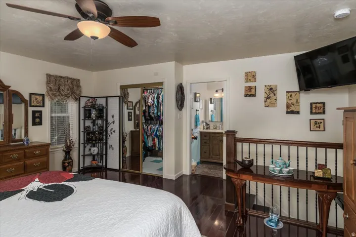 Room featuring dark wood-finish flooring, a ceiling fan with integrated lighting, and a window with blinds and valance