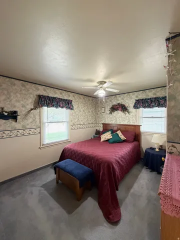 Bedroom featuring plush gray carpeting, two windows with valances, and a ceiling fan with integrated lighting