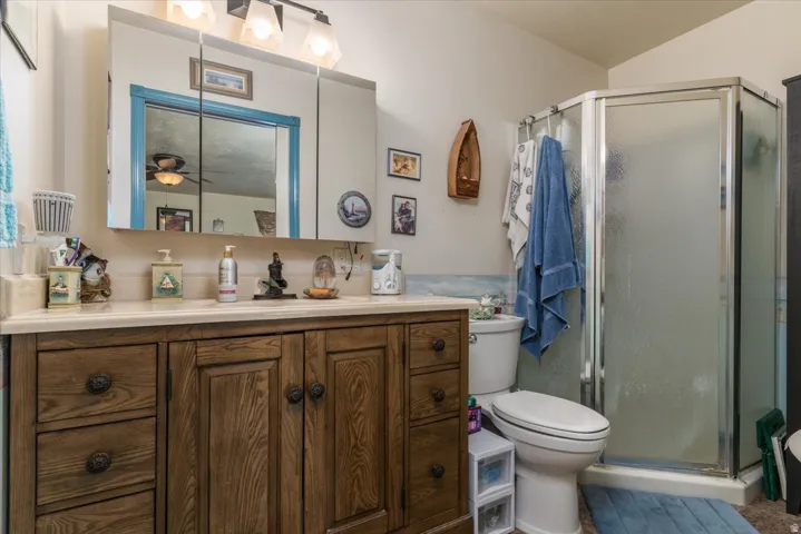 Bathroom featuring a wood-finish vanity with a light-toned countertop, a mirrored medicine cabinet, a three-light vanity fixture, and a glass-enclosed shower stall
