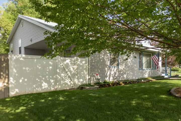 Siding exterior with a covered porch, white privacy fence, and a manicured lawn