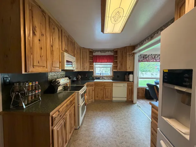 Kitchen featuring extensive wood cabinetry, dark countertops, built-in microwave, integrated dishwasher, and a double oven