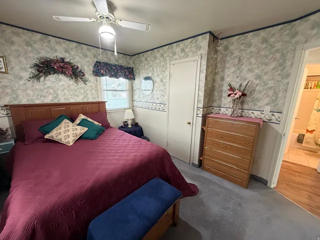 Carpeted room featuring a white ceiling fan with integrated lighting, a window, and a door