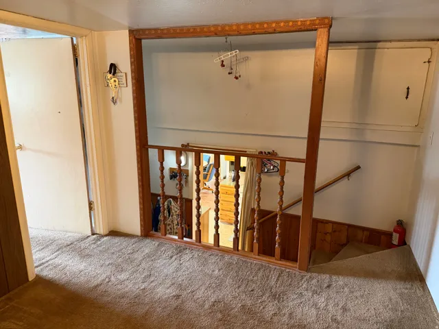 Carpeted landing with white walls and a wood-toned railing, featuring a solid door with a brass-toned knob