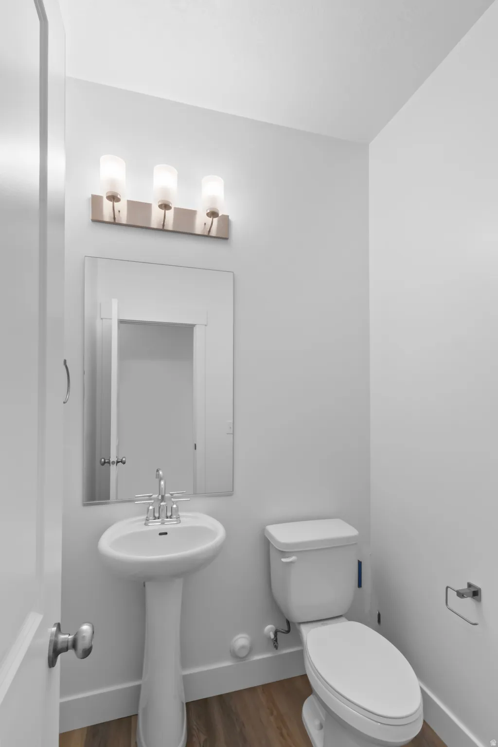 Pedestal sink with chrome faucet, toilet, and a three-light vanity fixture over a framed mirror