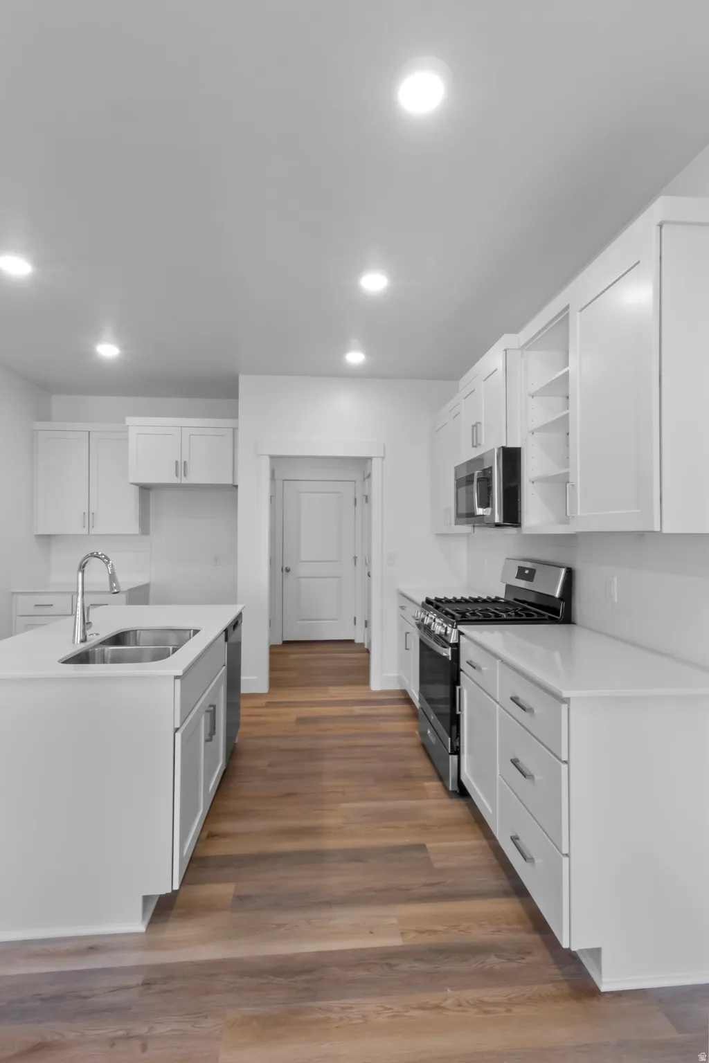 Contemporary kitchen featuring wood-finish flooring, white cabinetry, a center island with an undermount sink, stainless steel appliances, and recessed lighting