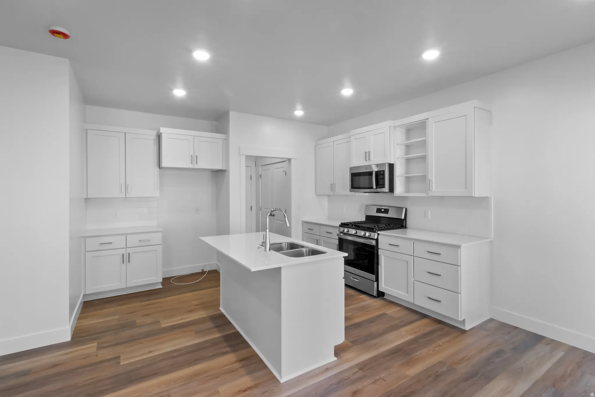Modern kitchen featuring white shaker cabinetry, stainless steel appliances, a center island with sink, white countertops, and wood-finish flooring
