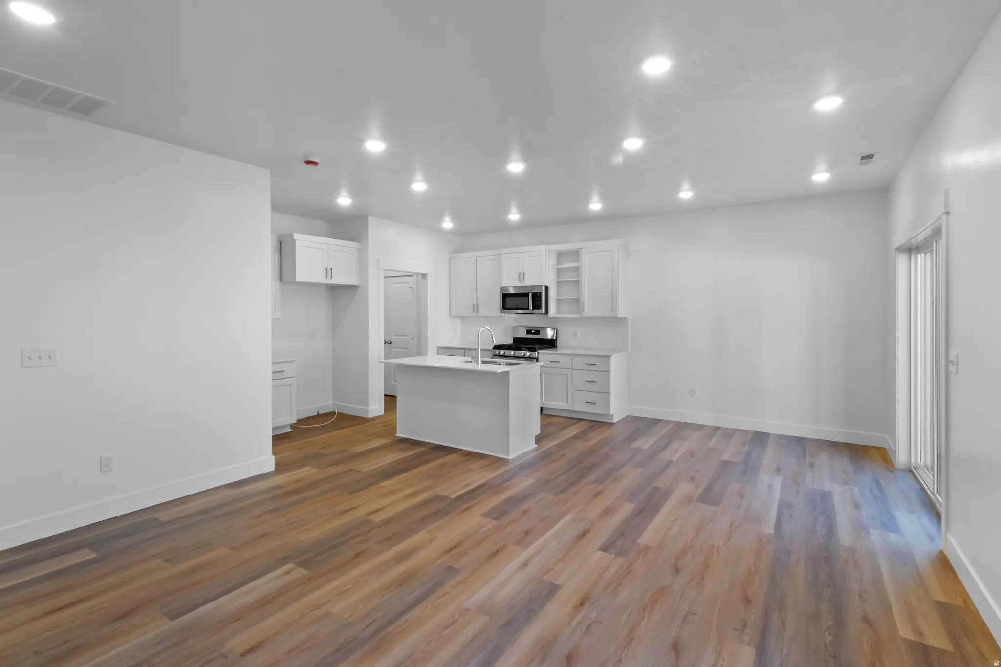 Open-concept living space featuring wood-finish flooring, recessed lighting, and a kitchen with white cabinetry