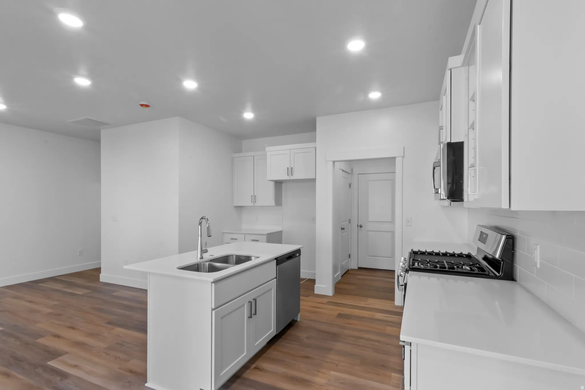 Modern kitchen featuring white cabinetry, light countertops, stainless steel appliances, a center island with a double sink, and wood-finish flooring