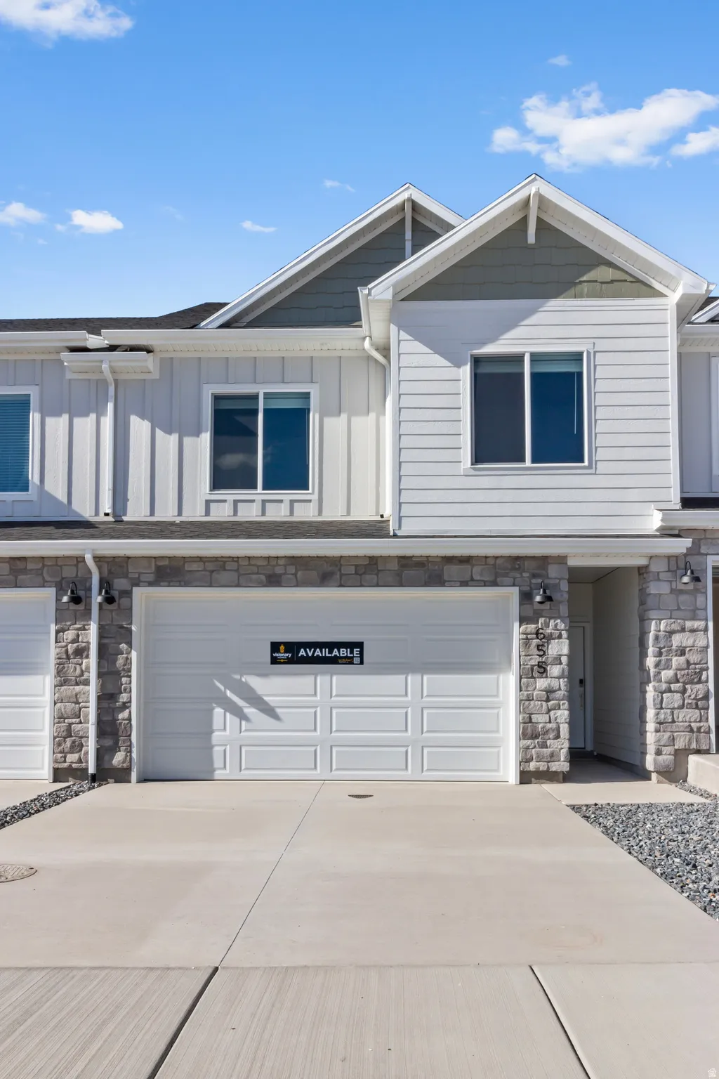 Modern townhome exterior featuring an attached garage, stone veneer accents, light siding, and a concrete driveway