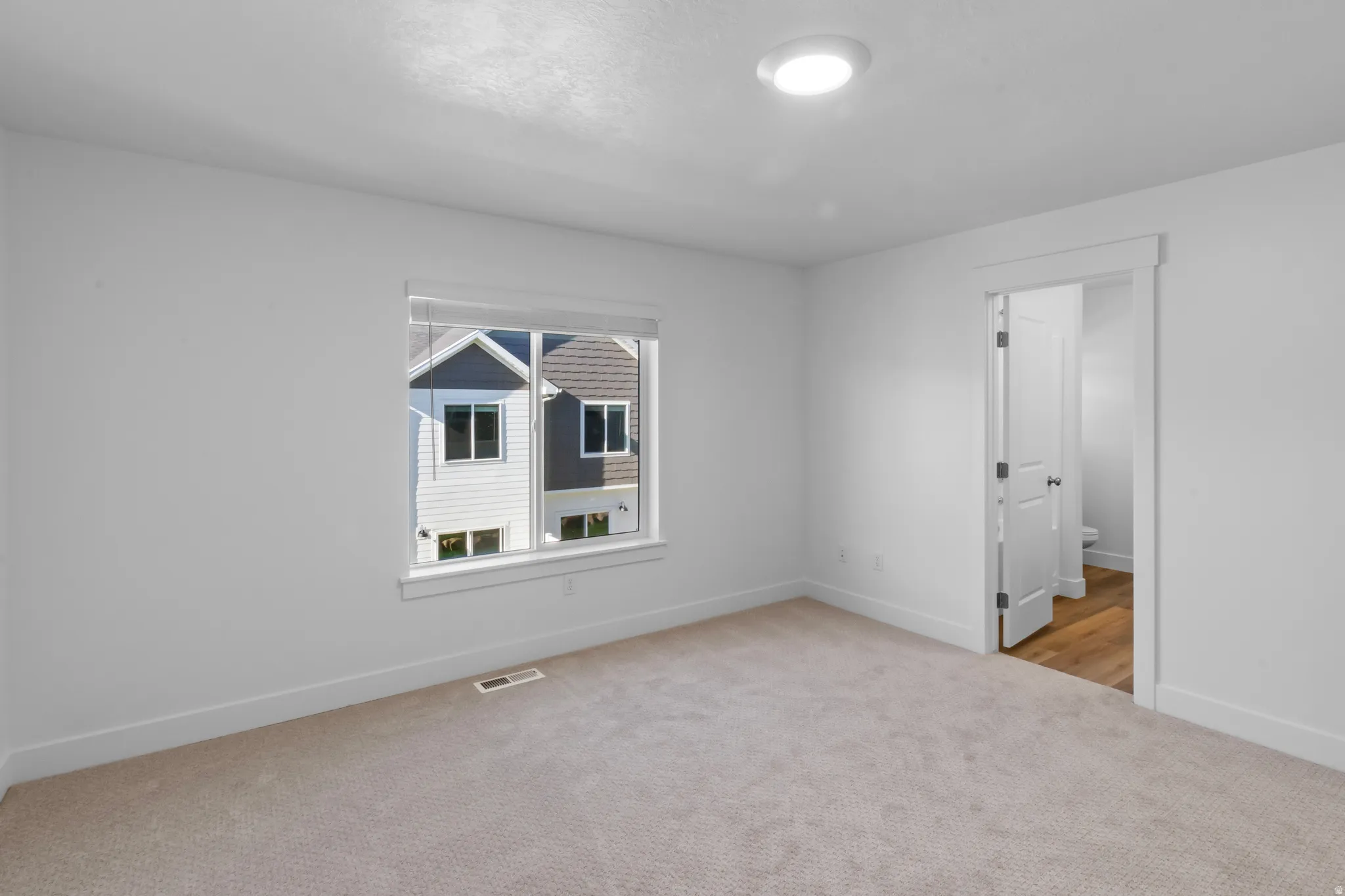 Carpeted room featuring a white-framed window with blinds, recessed lighting, and a white interior door with dark hardware