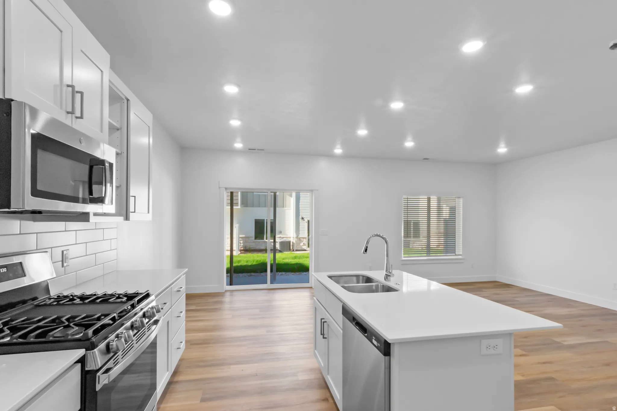 Modern kitchen featuring white cabinetry, subway tile backsplash, stainless steel appliances, and a central island with an undermount dual-basin sink