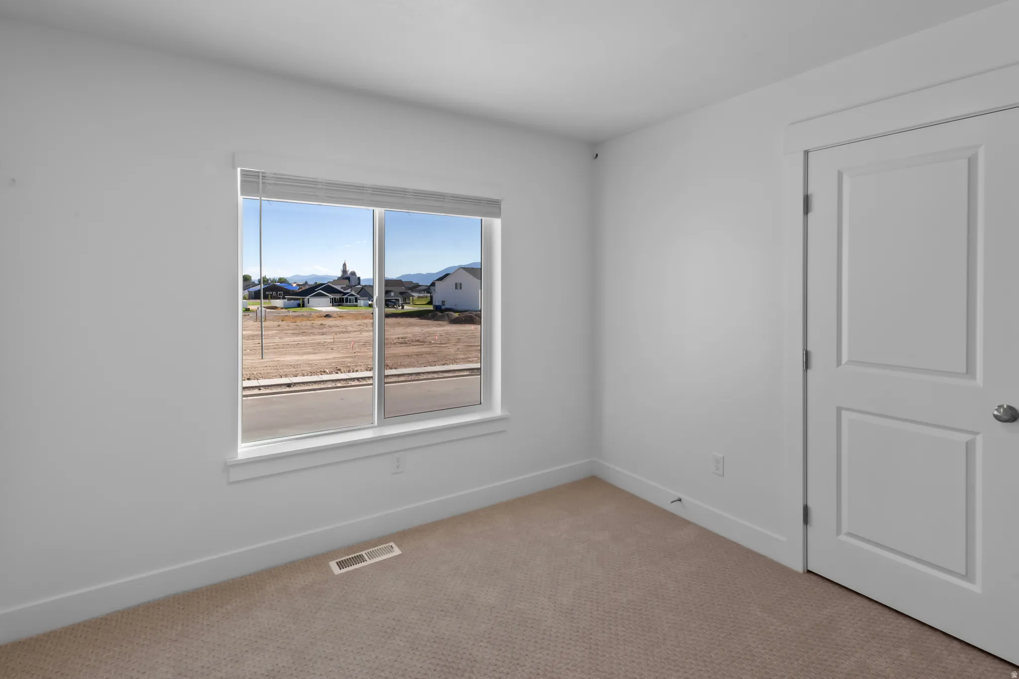 Bright interior room featuring a large window with white trim, neutral carpet flooring, and a paneled door